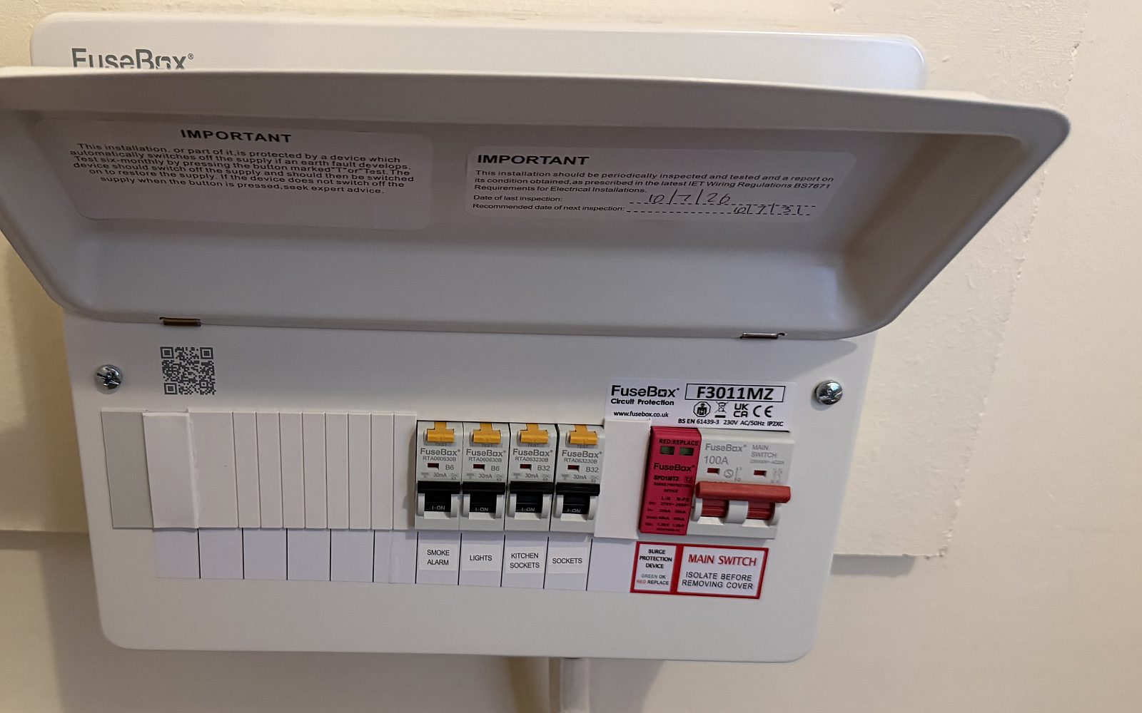 Newly fitted consumer unit with its lid lifted, showing labelled RCBOs, a surge protection device and the 100A main switch